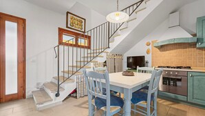 A dining area with a table and chairs, a staircase, a kitchen with a stove, and a television. - Villa 'Livia' with Shared Pool, Private Terrace and Garden (Sant'Anna Arresi)