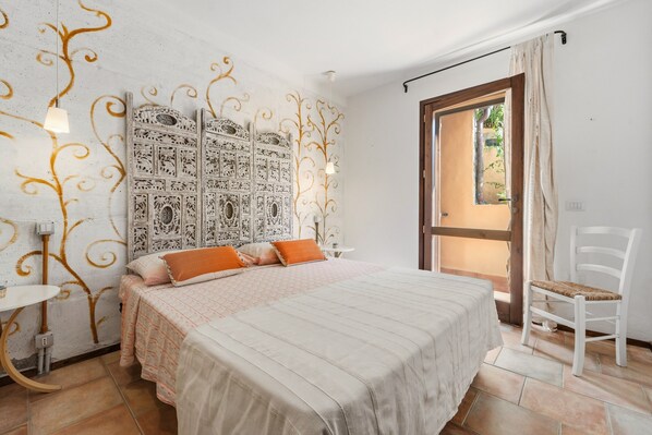 A bedroom with a bed, a chair, a small table, and a decorative headboard.