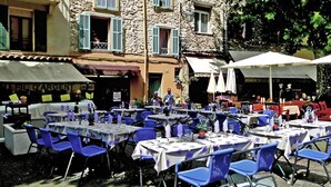 An outdoor café with tables and chairs, surrounded by stone buildings with shutters. - CASA-Noel villa avec piscine privée (Saint-Paul-de-Vence)