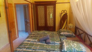 A bedroom with a bed, a wooden wardrobe, a nightstand, and a mosquito net. - Bed and breakfast (Glatigny)