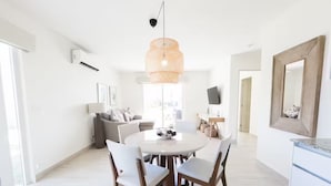 Un salon moderne avec une table à manger ronde, des chaises blanches, un canapé gris et un grand miroir au mur.