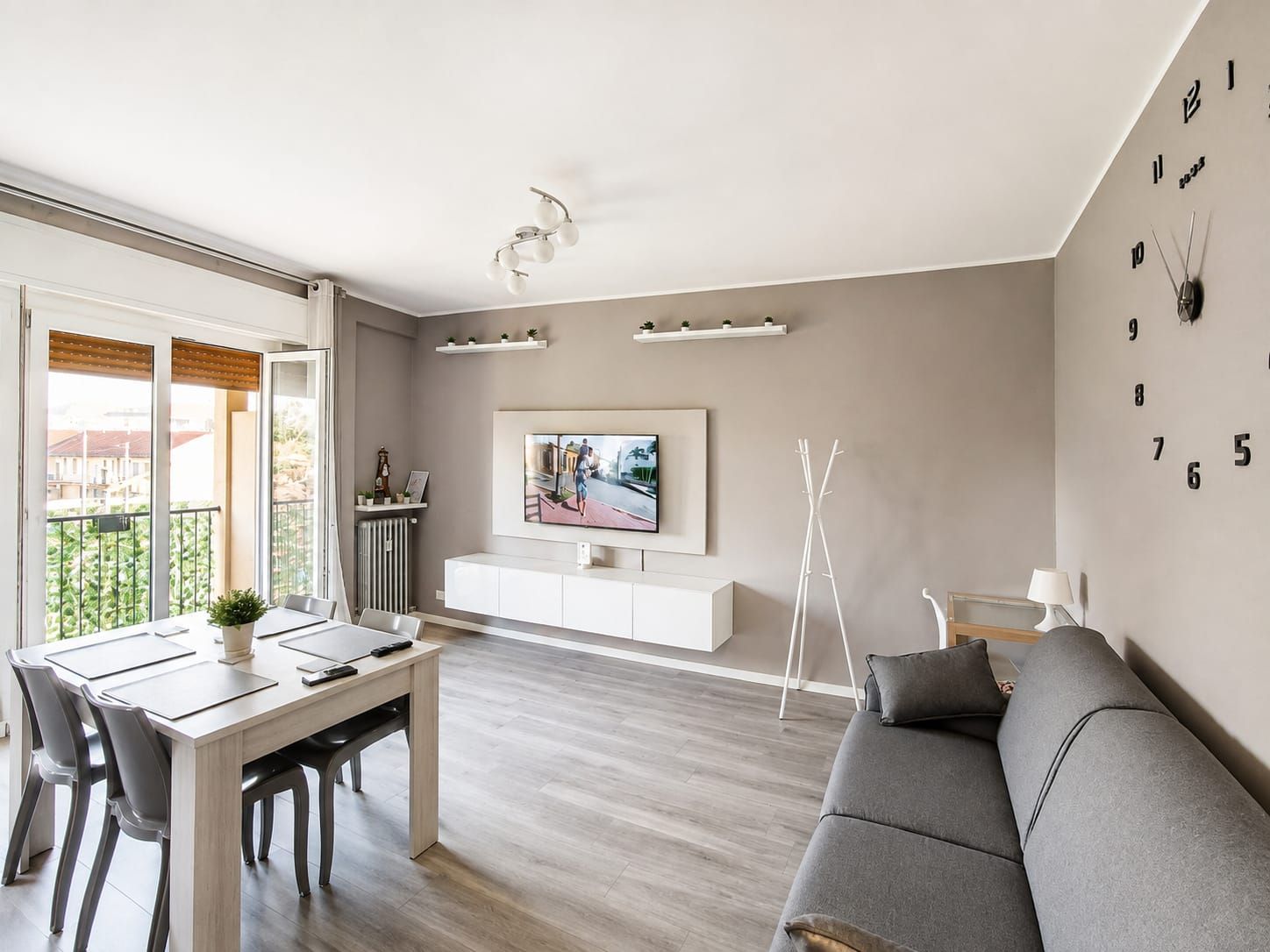 Un soggiorno moderno con un divano grigio, un tavolo da pranzo con sedie, una TV a parete e un balcone con vista.