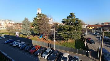 Un parcheggio con diverse auto, un'area giochi per bambini e il campanile di una chiesa sullo sfondo.