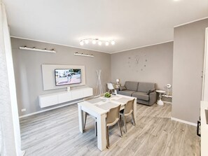 A modern living room with a dining area, a grey sofa, a flat-screen TV mounted on the wall, and a minimalist design.