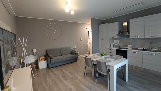 A modern living room with a grey sofa, a dining table with chairs, and a kitchen area with cabinets and a countertop. - Work & relax home paderno dugnano rho fiera (Paderno Dugnano)