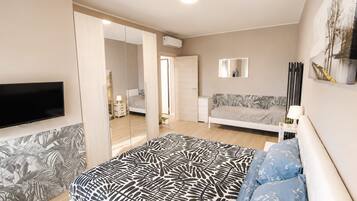 A bedroom with a bed, a TV, a sofa, a mirror, and a wall-mounted air conditioner.