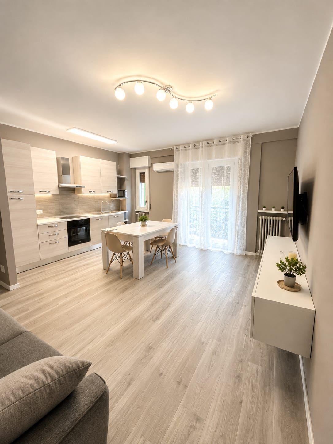 A modern kitchen with a dining area, a built-in oven, and a flat-screen TV mounted on the wall.