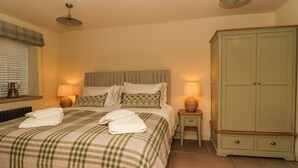 A neatly made bed with a plaid bedspread, two bedside lamps, and a green wardrobe in a hotel room. - Bridge House Cottage (Harrogate)