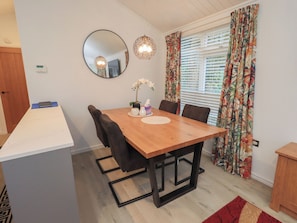 Un comedor con mesa de madera, sillas, un espejo y una ventana con cortinas.