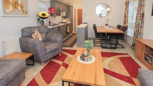 A compact living space with a grey sofa, a wooden dining table, and a kitchen area with modern appliances. - Merewood (Windermere)