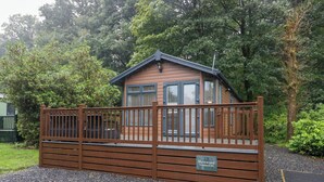 A wooden cabin with a fenced entrance, a small porch, and a sign indicating its name and location. - Merewood (Windermere)