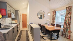 A modern kitchen with a dining area, including a wooden table and chairs, a red rug, and a mirror on the wall. - Merewood (Windermere)