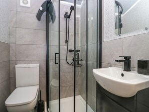 Ein modernes Badezimmer mit einer gläsernen Duschkabine, einer weißen Toilette und einem schwarzen Waschbecken mit Spiegel darüber.