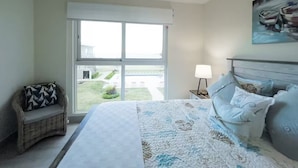 Un dormitorio con una cama grande, una ventana con vista a un jardín, un ventilador de techo y un cuadro en la pared.