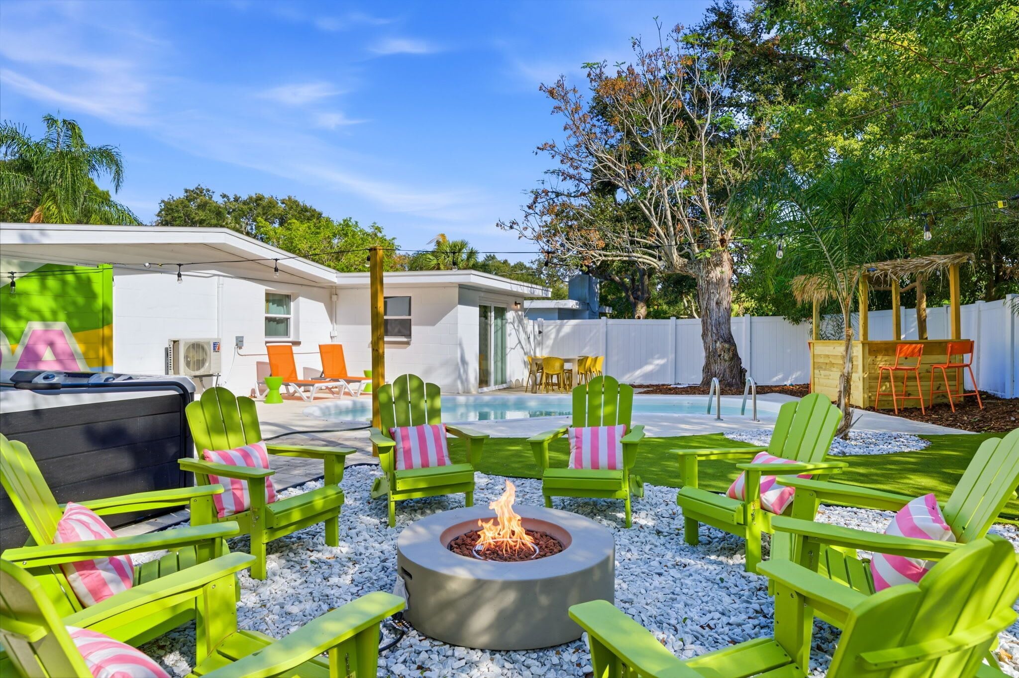 A backyard with a fire pit, green Adirondack chairs, and a pool.