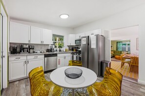 Una cocina moderna con armarios blancos, electrodomésticos de acero inoxidable y una zona de comedor con una mesa redonda y sillas amarillas.