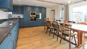 A modern kitchen with blue cabinets, a wooden dining table, and chairs. - Yr Hen Felin (Dyffryn Ardudwy)