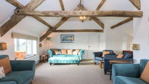 A spacious living room with a high ceiling and exposed wooden beams, featuring a large teal sofa, a smaller blue sofa, and a coffee table. - Yr Hen Felin (Dyffryn Ardudwy)