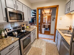A modern kitchen with stainless steel appliances, granite countertops, and a view into the dining area. - Autumn Mountain Stay Whistlepunk 32, 4BR + Loft (Snowshoe)