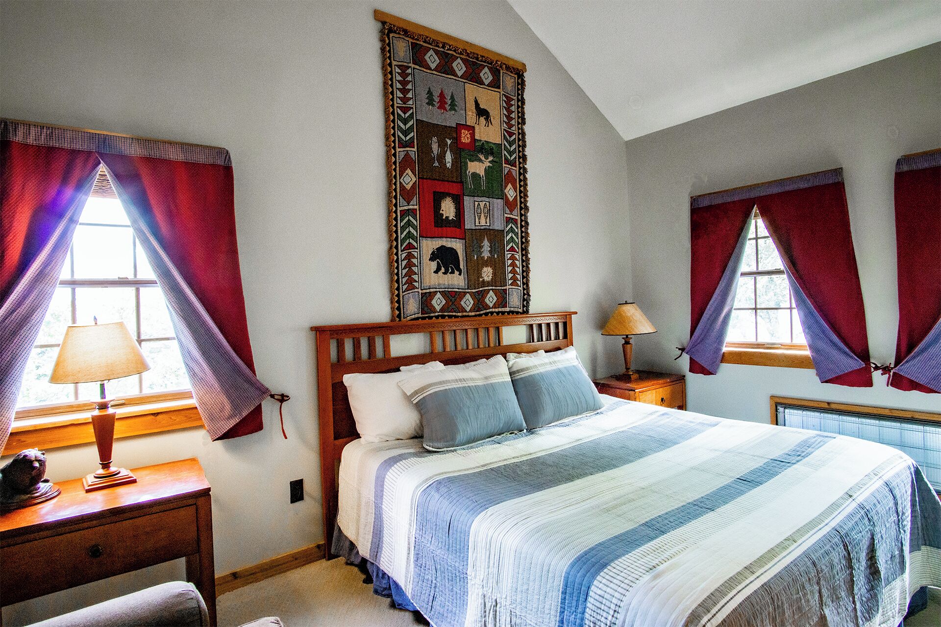 Een slaapkamer met een houten bed, rode gordijnen, een sprei en een wanddecoratie.