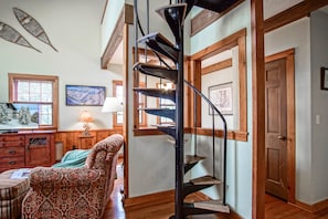 Uma escadaria em espiral em um quarto com piso de madeira, uma poltrona estampada e uma televisão.