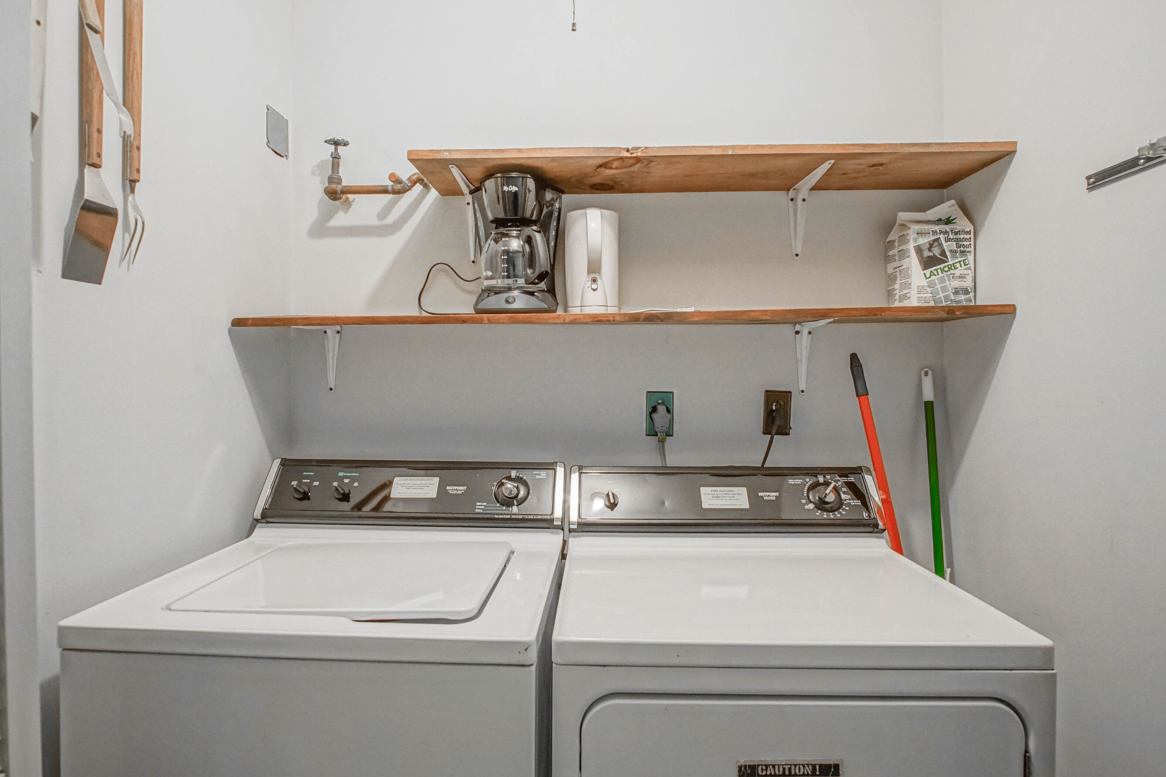 A laundry area with two white washers and dryers, a coffee maker, and a shelf with a newspaper.