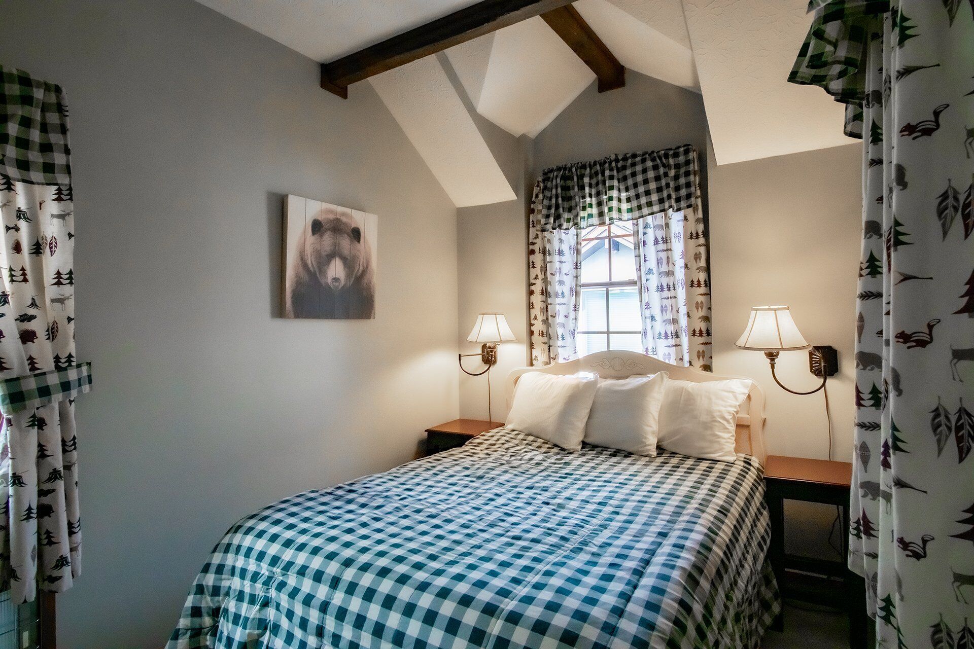 A bedroom with a bed, two bedside lamps, a window with curtains, and a bear painting on the wall.