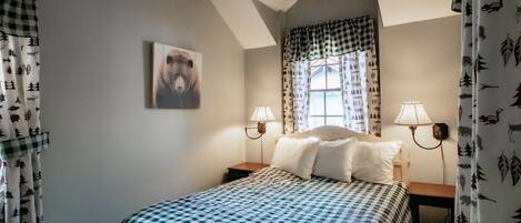 A bedroom with a bed, two bedside lamps, a window with curtains, and a bear painting on the wall.