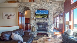 A cozy living room with a stone fireplace, leather sofas, and a large TV screen above it. - Slope Side 8 BR at Sanctuary Majestic Mountain Top Estate 4800 Square Feet of Quality Sleeps 16 (Snowshoe)
