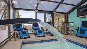 Uma área de piscina com cobertura de vidro, cadeiras de lounge azuis e borda de piscina em azulejo.
