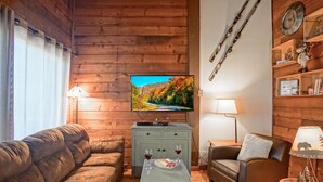 Een knus houten interieur met een televisie bevestigd boven een lichtblauwe kast, een bruine leren bank, een bruine leren fauteuil en een kleine tafel met een bord en glazen.