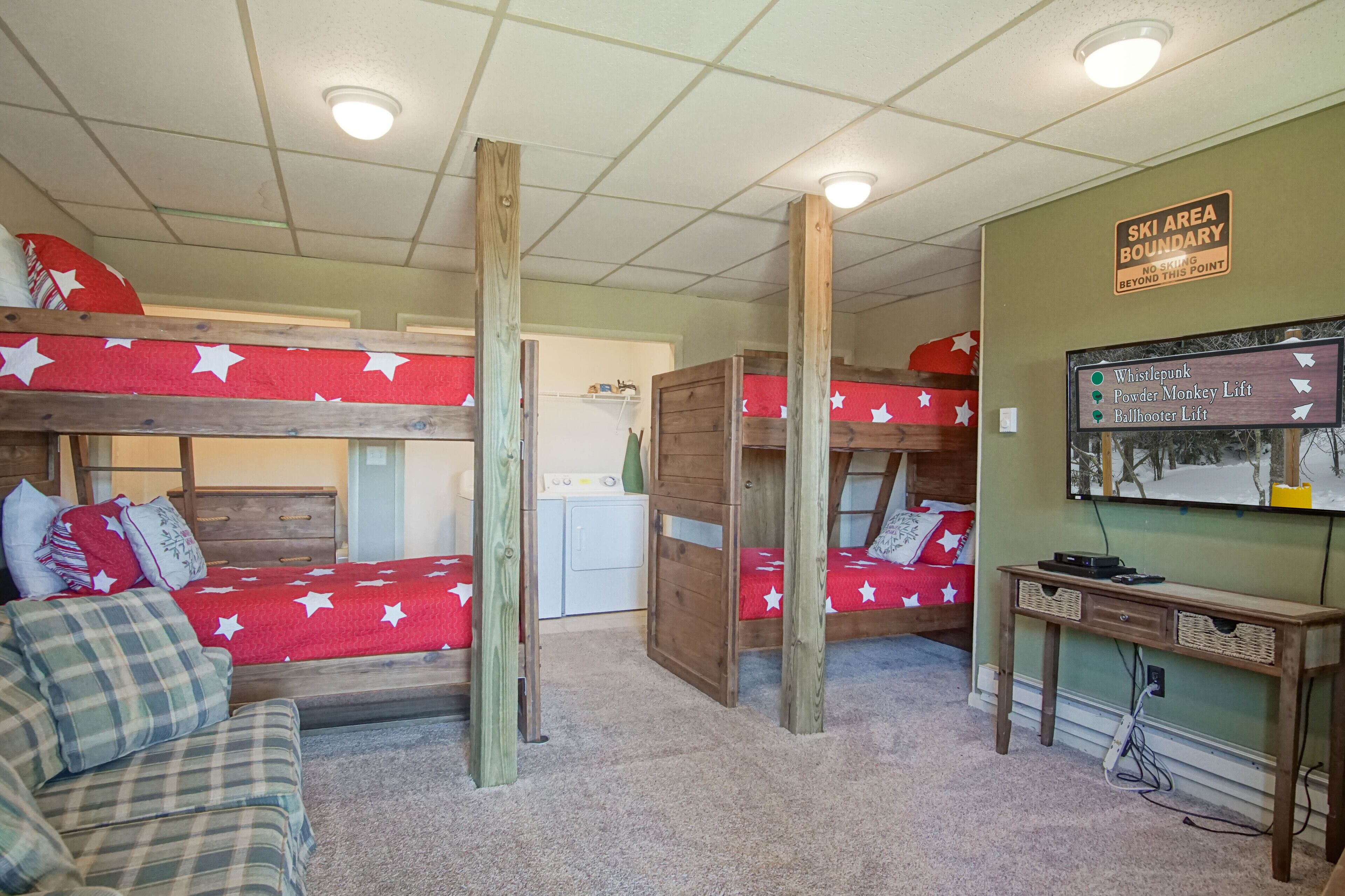 Een slaapkamer met stapelbedden, een bord dat het skigebied markeert, een wasmachine en een bureau met een beeldscherm.