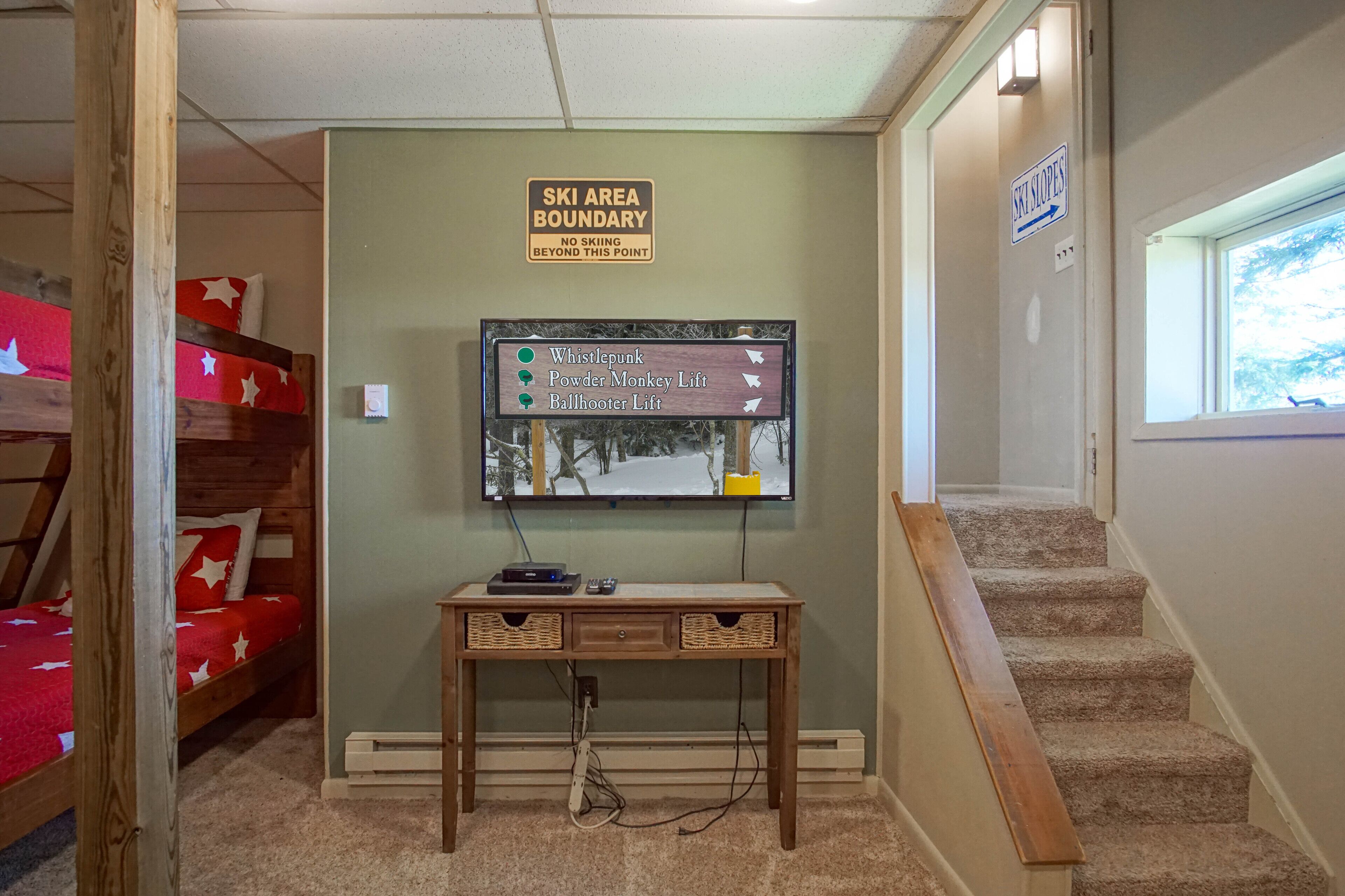 A hotel lobby with a wooden desk, a sign indicating a ski area boundary, and a wall-mounted TV displaying ski slopes.