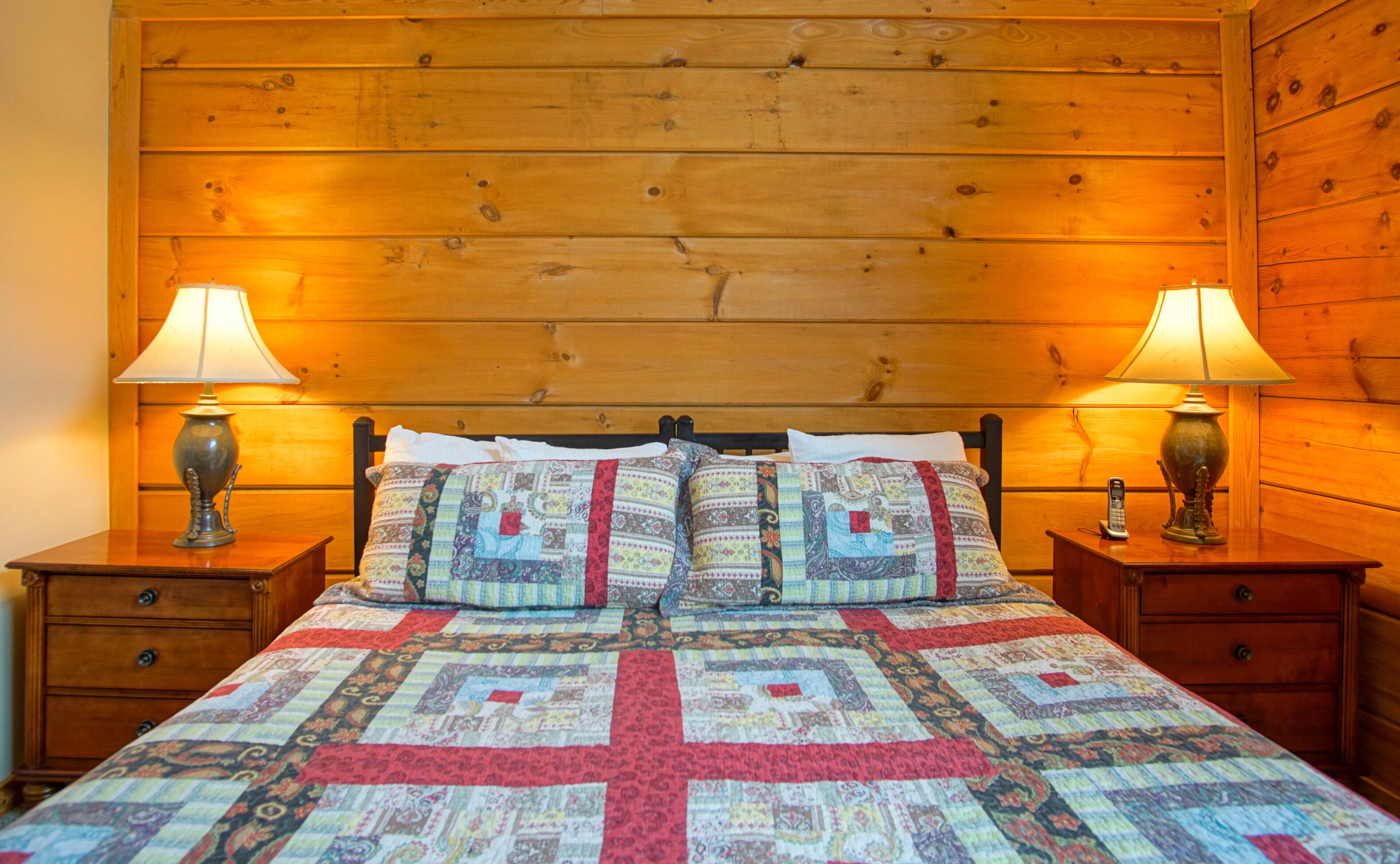 A wooden-paneled room with a bed, two bedside tables, and two lamps.