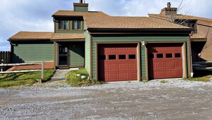 A two-story house with a green exterior, a brown roof, and two red garage doors. - Lands End 4 BR Condo: 5 Mins Walk to the Village (Snowshoe)