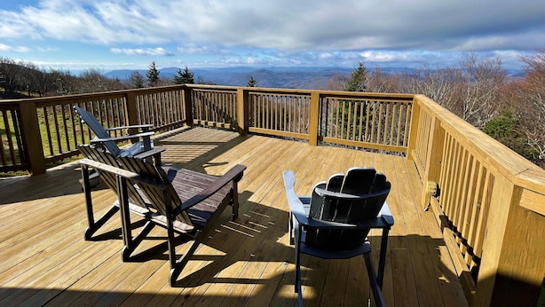 A wooden deck with two Adirondack chairs and a table, overlooking a mountainous landscape. - Lands End 4 BR Condo: 5 Mins Walk to the Village (Snowshoe)