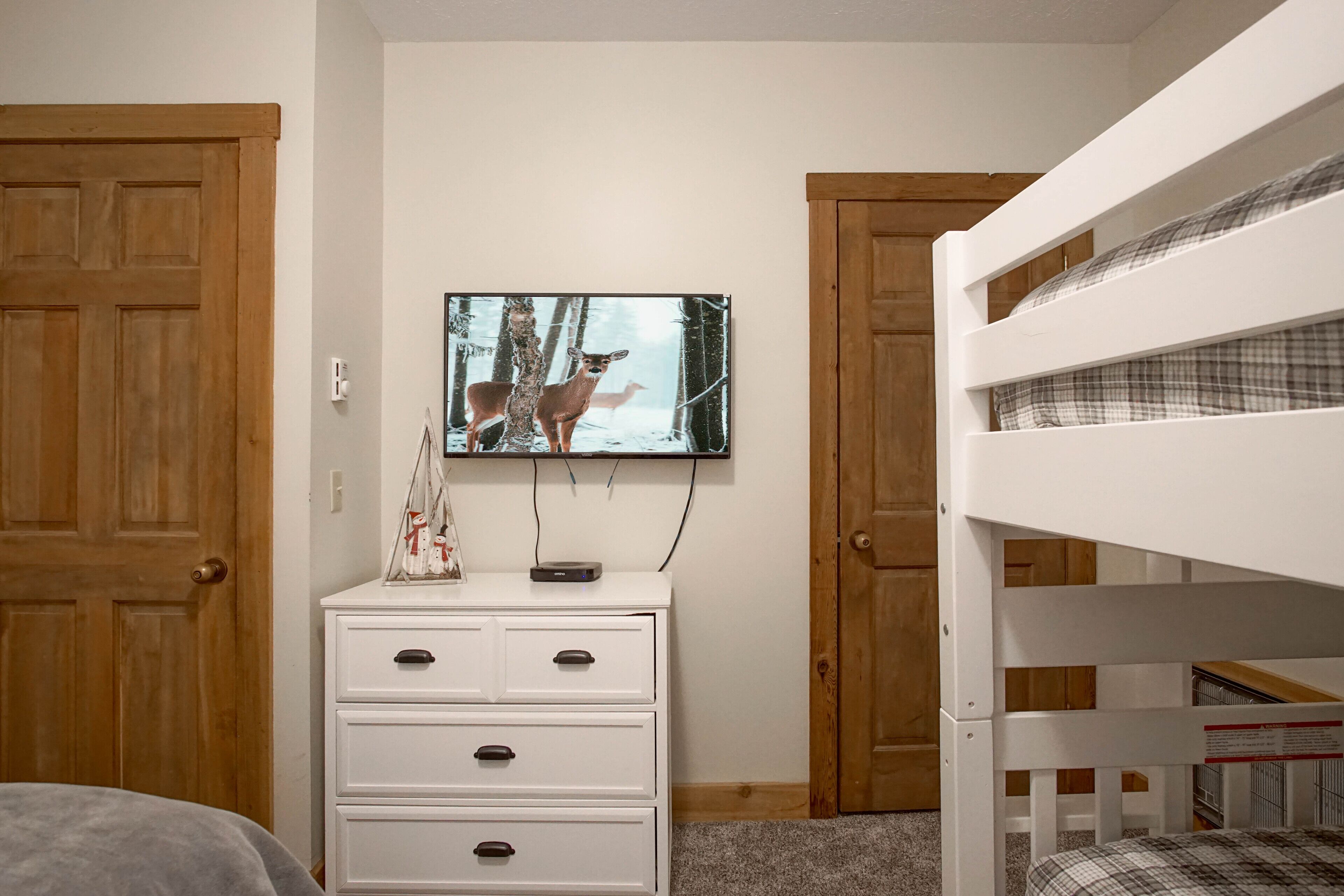 Un dormitorio con una cama litera, un aparador, un televisor montado en la pared y puertas de madera.