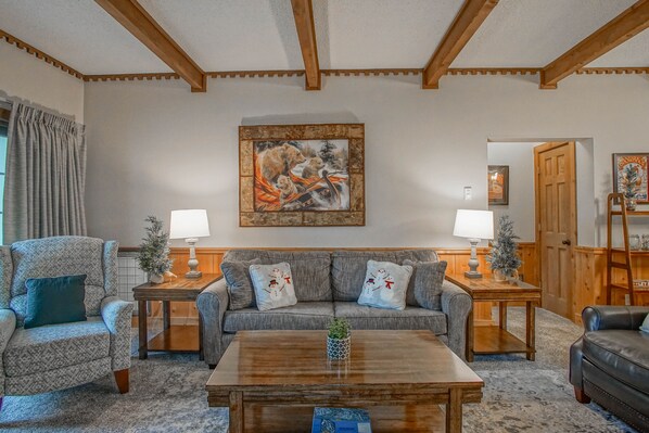 A living room with a grey patterned sofa, two side tables with lamps, a wooden coffee table, and a painting of a bear on the wall. - Whistlepunk # 28: 2 Bedrooms, 2 Full Baths: Slope Side. Wood Fireplace. Central Location (Snowshoe)