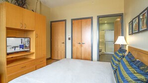 Een hotelkamer met een bed, een televisie op een houten kast en een douchecel zichtbaar achter een glazen deur.