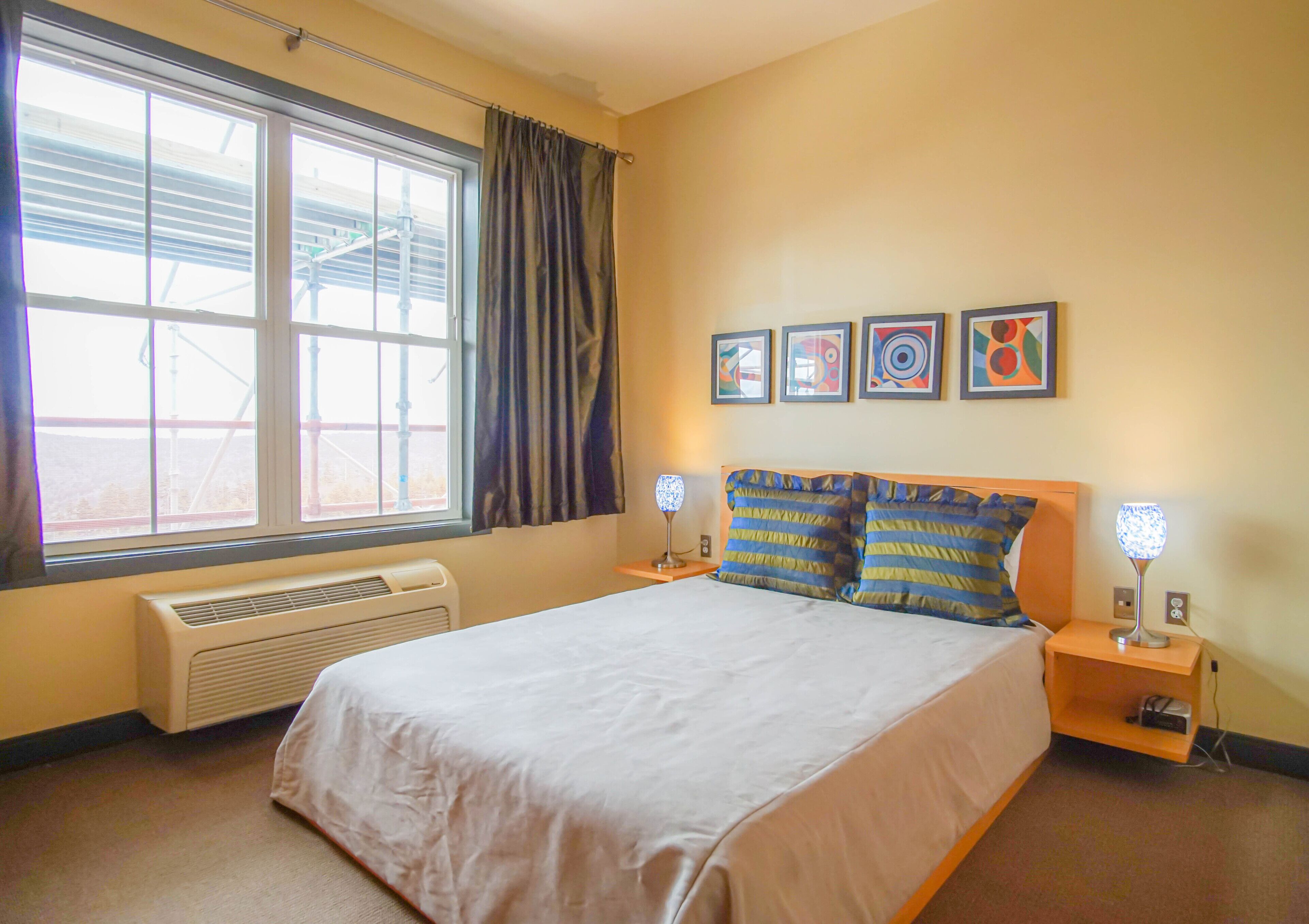 Ein Hotelzimmer mit einem großen Bett, einem Fenster mit Vorhängen, einem Heizkörper und drei an der Wand befestigten Bilderrahmen.