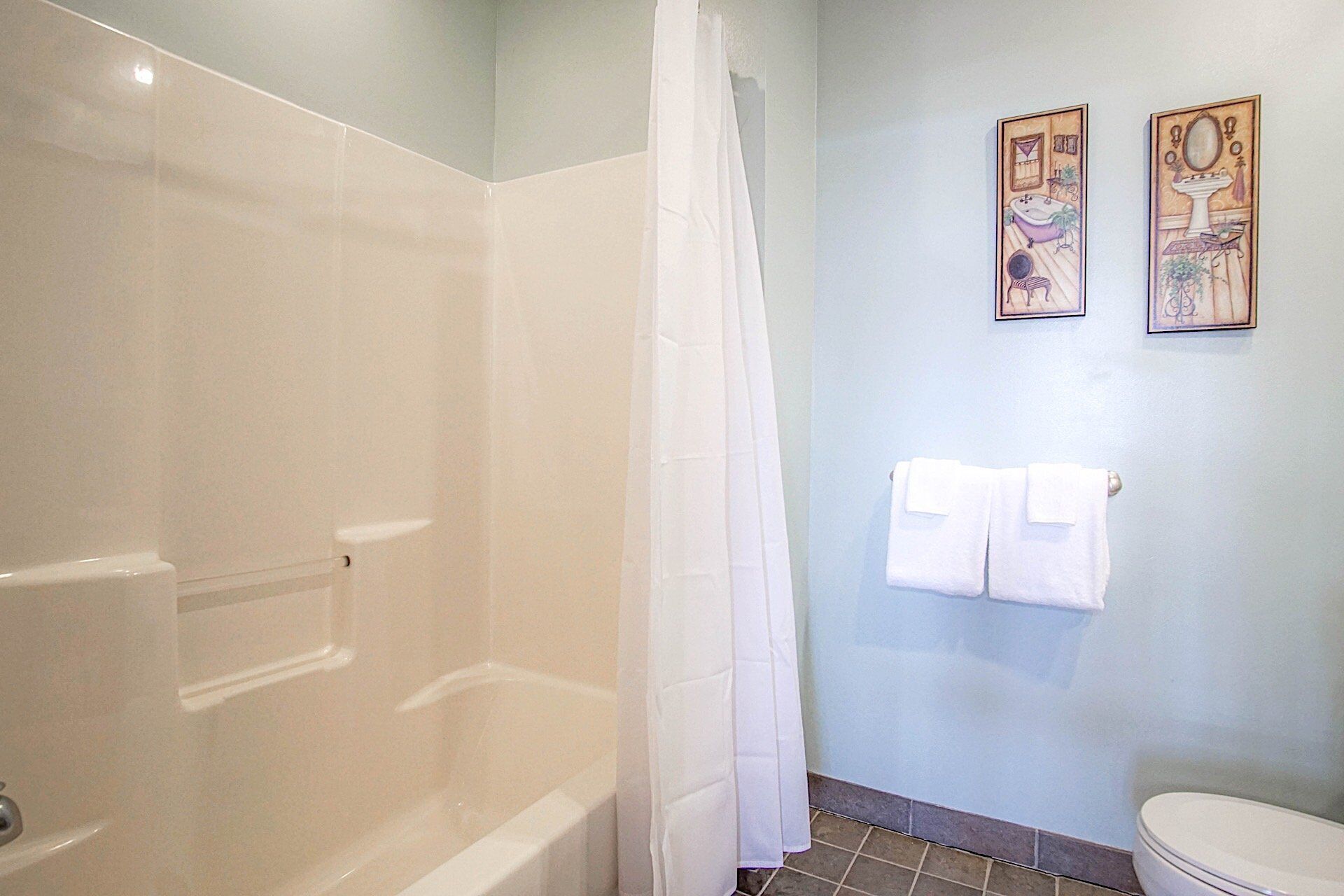 A bathroom with a shower, toilet, and two framed pictures on the wall.
