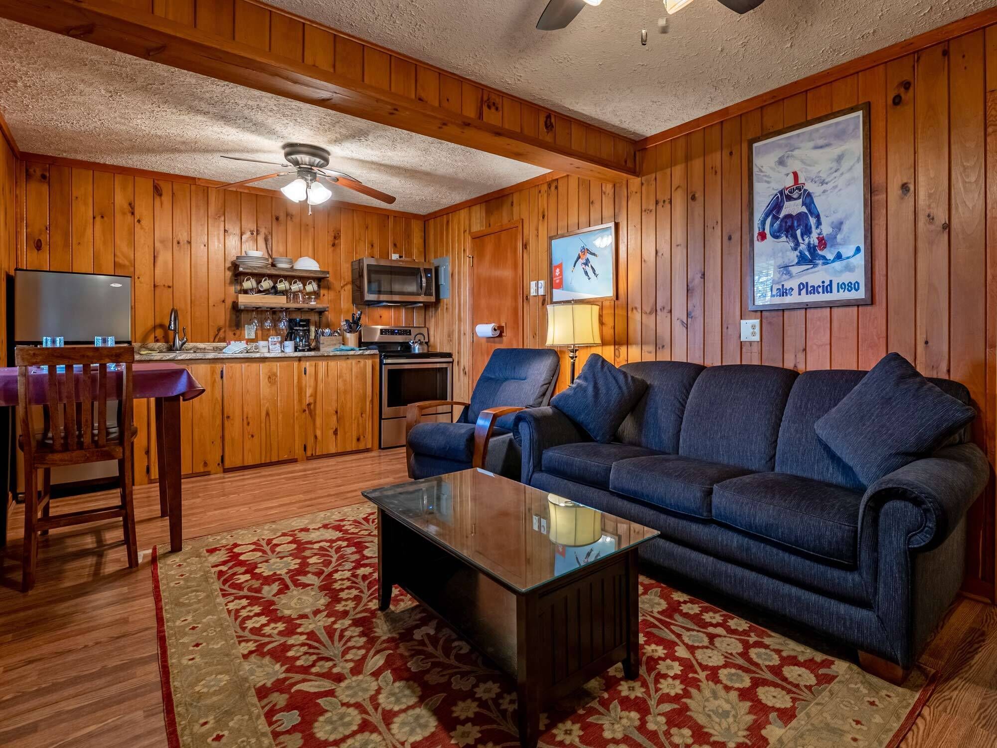 A cozy cabin interior with a wooden interior, a dining area, a kitchen, and a living room with a sofa and a coffee table.