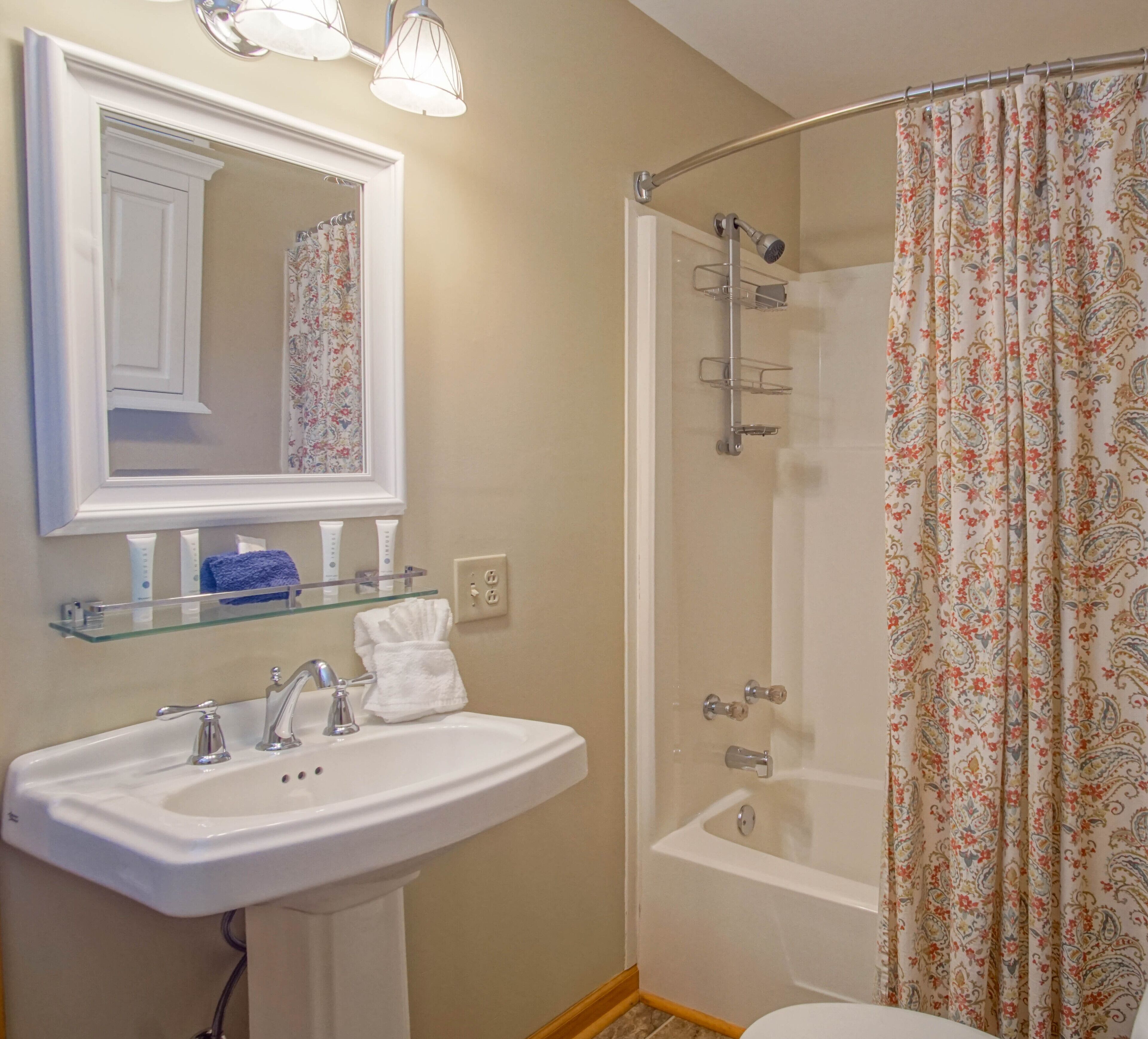 Un baño con lavamanos blanco, espejo y cortina de ducha.