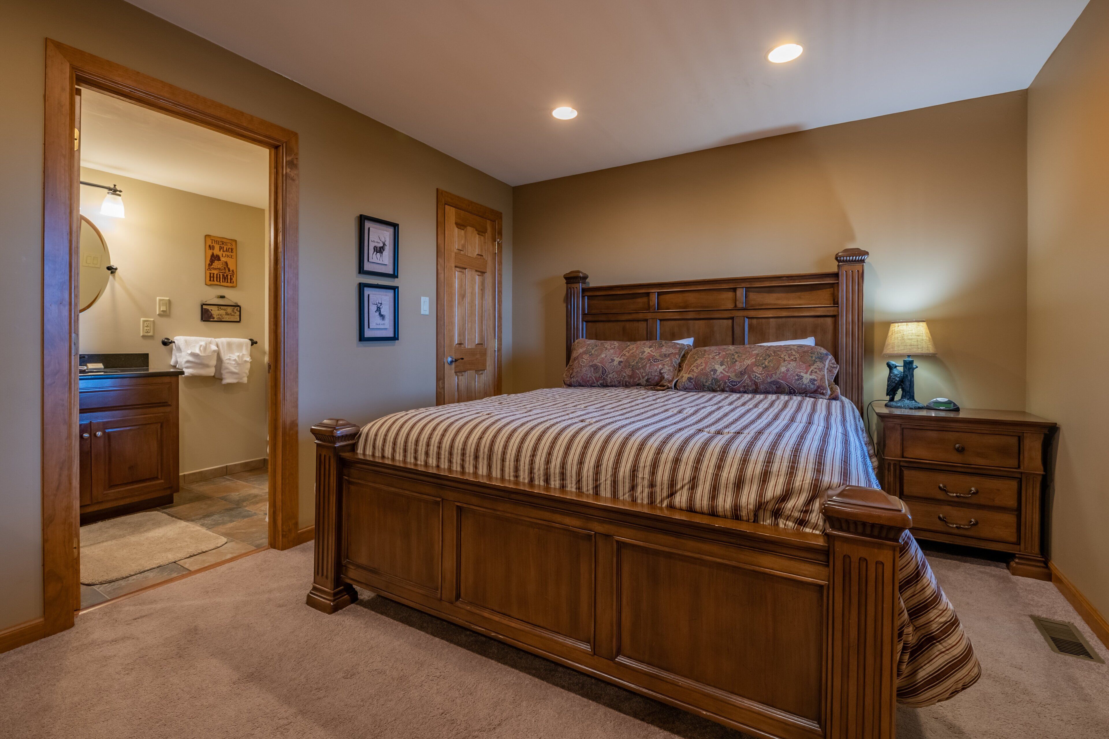A bedroom with a wooden bed, a nightstand, a lamp, and a bathroom visible through an open door.