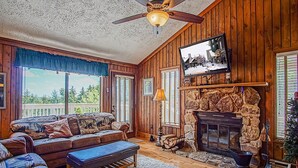 A cozy living room with a fireplace, wooden walls, and a large window overlooking a scenic view. - Wabasso 10 Ski Hideaway Outside Your Door 2 Br Spacious Balcony (Snowshoe)