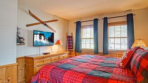 Ein Schlafzimmer mit einem Bett, einem Schreibtisch, einem Sessel, einem Fernseher und einem Fenster mit Vorhängen.