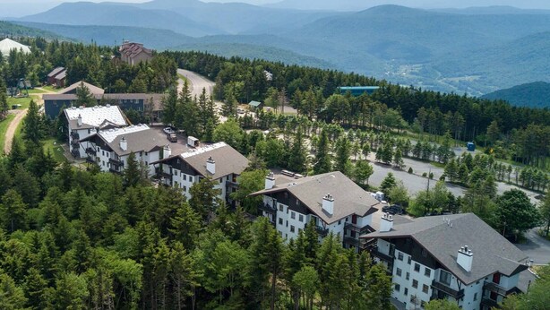 Ein Resort mit mehreren Gebäuden, umgeben von dichtem Wald und Bergen im Hintergrund.