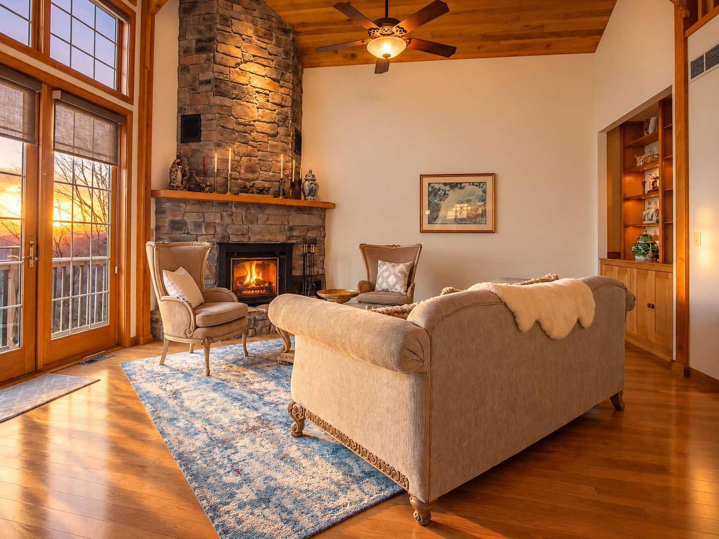 A cozy living room with a stone fireplace, two armchairs, a sofa, and a large window with a view.