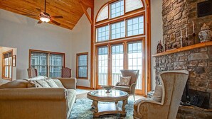 A spacious living room with a stone fireplace, large windows, and a ceiling fan. - Top Property on Snowshoe Mountain North Westridge 32 is as Magnificent as its Western Views! (Snowshoe)