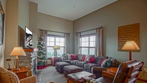 A cozy living room with a sectional sofa, a plaid armchair, and a wooden coffee table. A Christmas tree is visible in the corner, and there are two lamps on side tables. - 3 Bedroom, 2 Full Baths, Slope Side. Outdoor Hot Tubs on Site. Ski Lift Overlook (Snowshoe)